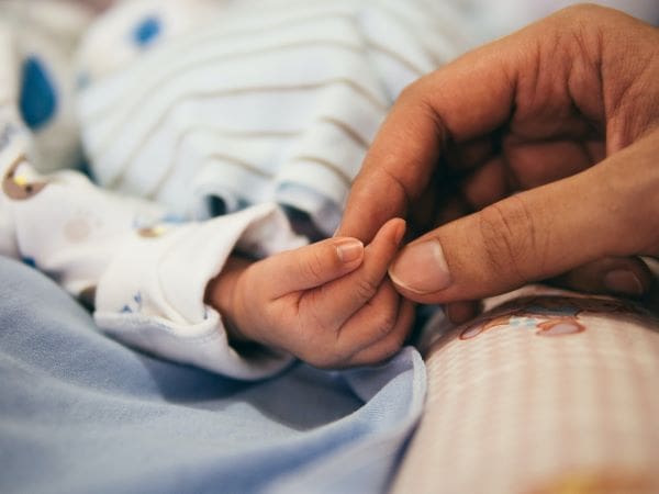 An adult holding a newborn baby's hand.